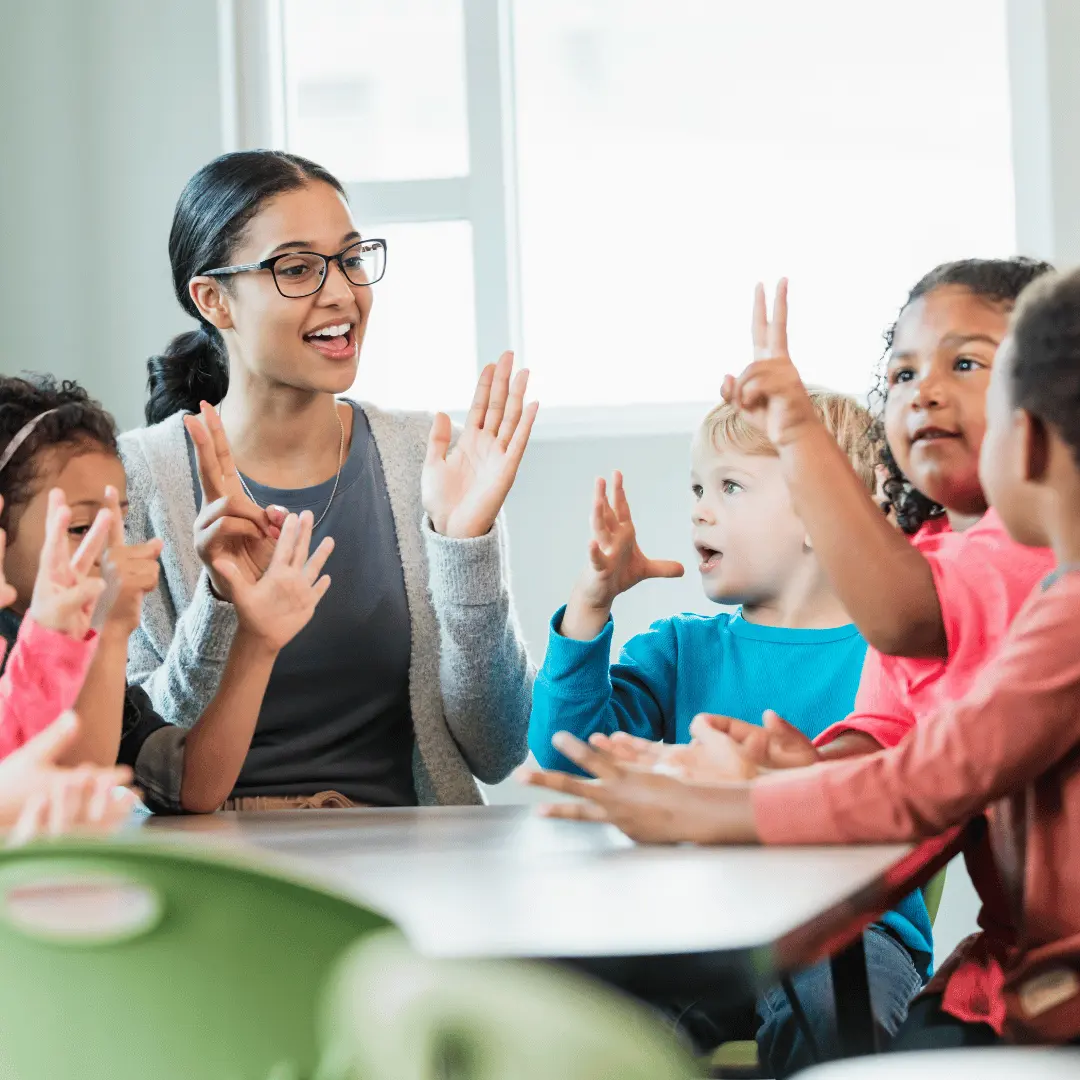 Teacher leads an active classroom discussion as diverse kids raise their hands to answer a question.